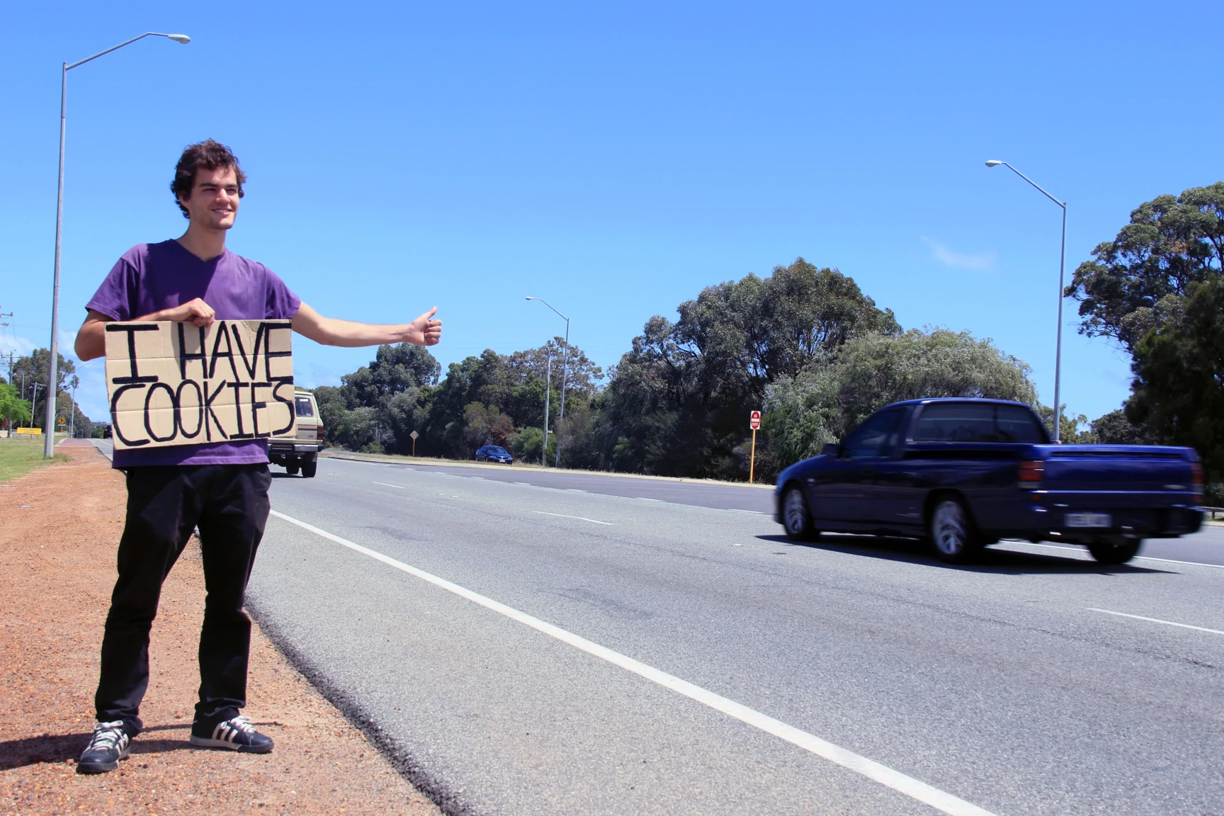 Young man hitchhiking with a sign that reads 'I have cookies'.